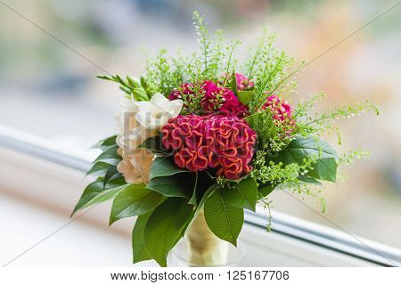 Wedding bouquet on window sill. Bride's traditional symbolic accessory. Floral composition with red celosia flowers.