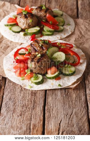 Grilled meat balls with fresh vegetables on a flat bread close up. Vertical