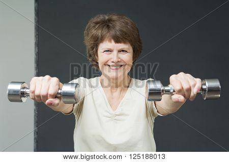 Smiling fit aged lady with exercise dumbbells