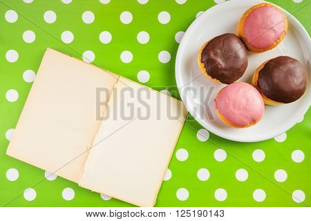 Vintage notebook with recipe for delicious homemade doughnuts with topping top view of cookbook with blank pages as copy space and tasty donuts on a plate over polka dotted surface.