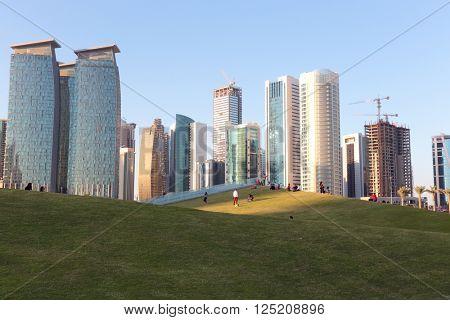 DOHA, QATAR - FEBRUARY 9, 2016: Residents relax on the newly finished artificial grass-covered hills of Hotel Park, in the shadow of the commercial towers of the Dafna district of the Qatari capital