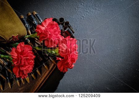 Carnations with forage-cap and ammunition belt on dark background