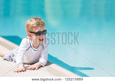 smiling excited boy in sunglasses and rashguard enjoying warm weather in swimming pool vacation and sun protection concept