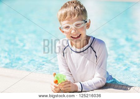 smiling excited boy with beach toy in goggles and rashguard enjoying warm weather in swimming pool vacation and sun protection concept