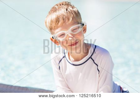 smiling excited boy in goggles and rashguard enjoying warm weather in swimming pool vacation and sun protection concept