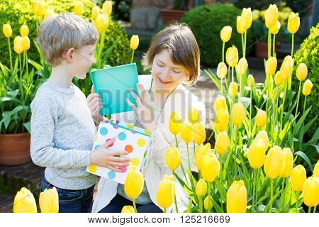 happy smiling mother and her loving son giving a present and spending time together in the beautiful blooming park at spring time, mother's day concept