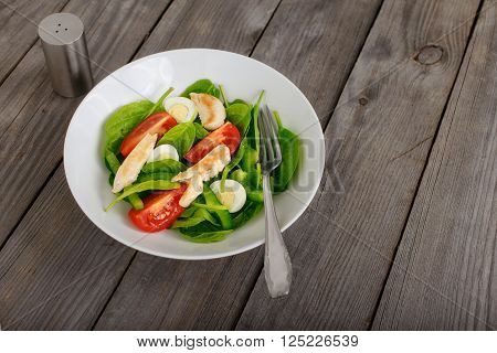 Fresh salad with spinach leaves tomato cucumber and quail eggs in ceramic white plate on a wooden rustic table top view with copy space. Healthy food