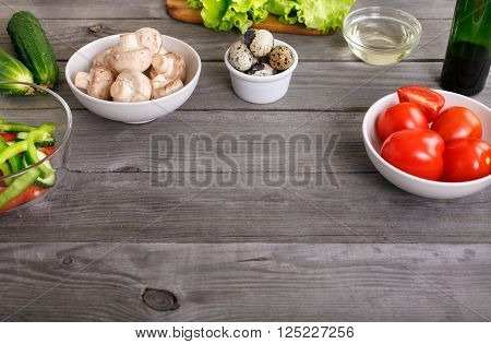 Ingredients for cooking healthy food. Tomatoes peppers cucumber mushrooms salad oil and quail eggs on a wooden table. Top view with copy space