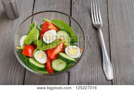 Fresh salad with spinach leaves, tomato, cucumber and quail eggs in glass bowl on a wooden rustic table, top view with copy space. Healthy food