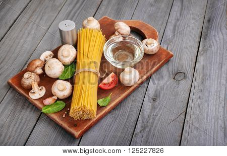 Italian spaghetti on a wooden board on a wooden rustic table with mushrooms, tomato, oil and spinach leaves. Top view with copy space