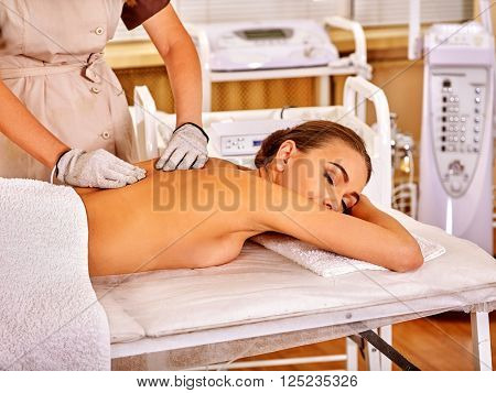 Young white relaxed woman  receiving electric massage at beauty salon. Beautician wearing electricity gloves. In room is device for hardware cosmetology. 