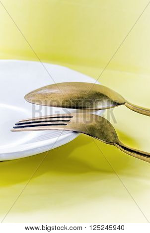 Old brass spoon and fork on the dish yellow backgroundsoft focus