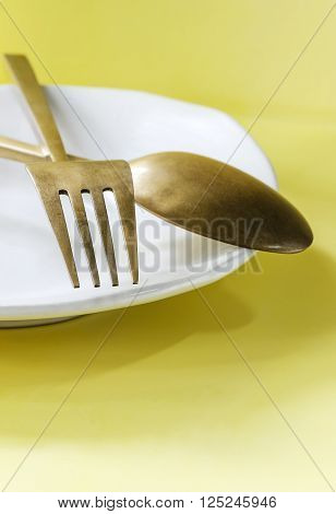 Old brass spoon and fork on the white dish yellow backgroundsoft focus