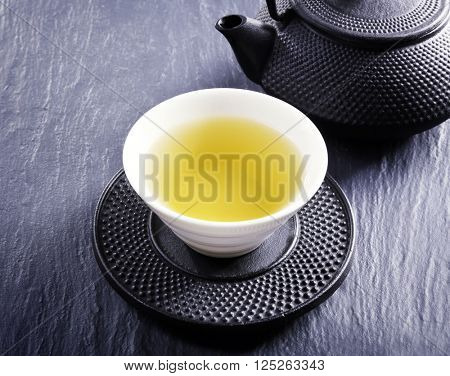 Pouring green tea into white pialat on slate plate background