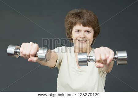 Smiling fit aged lady with exercise dumbbells