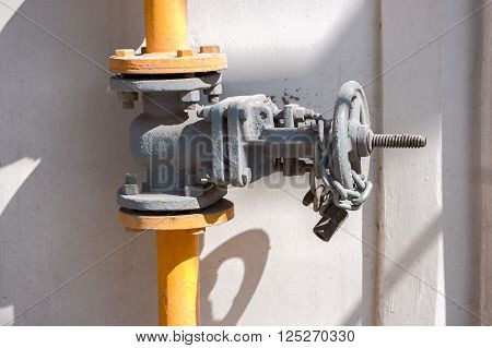 Natural gas valve on steel pipe painted in yellow with shadows.