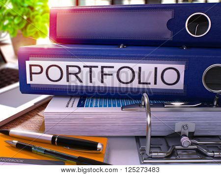 Blue Ring Binder with Inscription Portfolio on Background of Working Table with Office Supplies and Laptop. Portfolio Business Concept on Blurred Background. 3D Render.