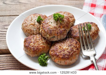 Fresh fried cutlets in a white plate on wooden table.