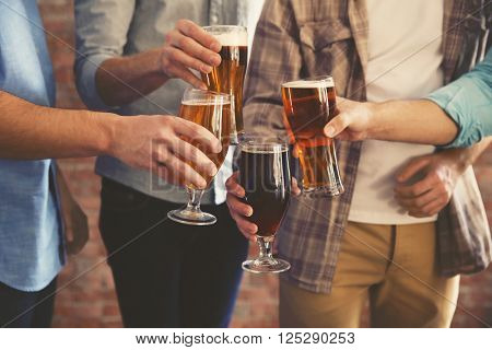 Male group clinking glasses of dark and light beer on brick wall background