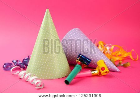 Two dotted Birthday hats with serpentine streamer and noise makers on pink background