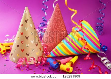 Three Birthday hats with serpentine streamer and noise makers on purple background