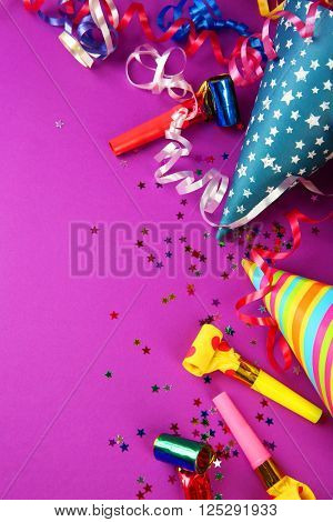 Birthday hats with serpentine streamer and noise makers on purple background