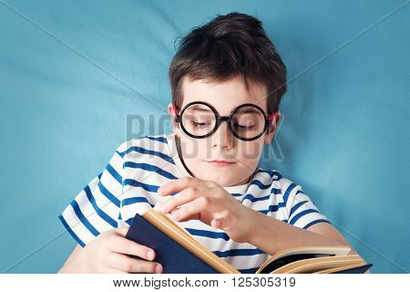 seven years old child lying with book on blue background