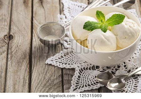 Vanilla ice cream with mint leaves in white bowl on rustic wooden background, selective focus, copy space