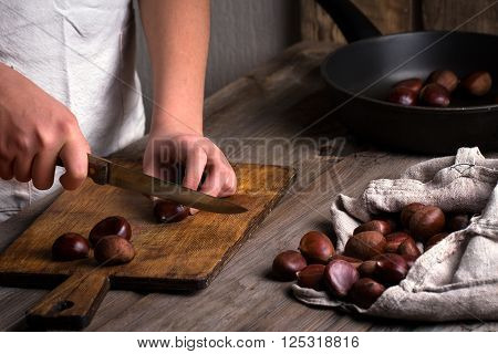 woman cuts roasted chestnuts on old wooden cutting board