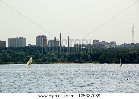 two windsurfers surf in lake in the city