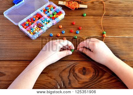 Children hands holding beads and cord. Baby sensory game