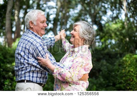 Cheerful senior couple dancing against trees in back yard