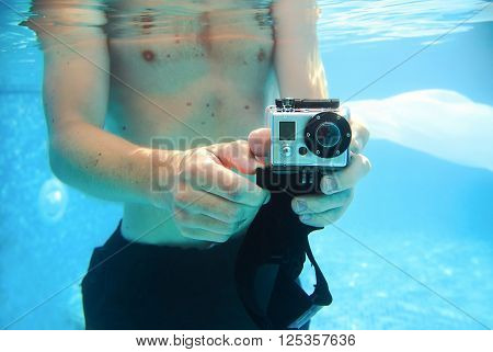 young man taking pictures underwater in the swimming pool in summer