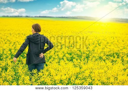 Woman agronomist standing in the field of blooming cultivated rapeseed plantation female agricultural expert controlling the growth of agricultural crops.