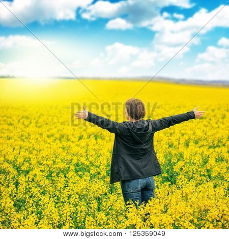Woman agronomist standing in the field of blooming cultivated rapeseed plantation female agricultural expert controlling the growth of agricultural crops and looking to distant point on the horizon.