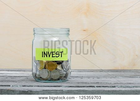 Label on a glass jar with the inscription - invest. Glass jar with coins. Financial concept on wooden background