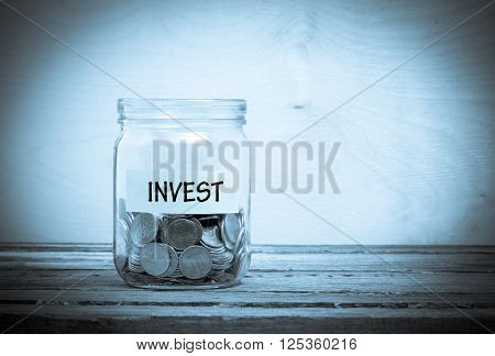 Label on a glass jar with the inscription - invest. Glass jar with coins. Financial concept on wooden background