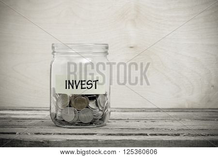 Label on a glass jar with the inscription - invest. Glass jar with coins. Financial concept on wooden background
