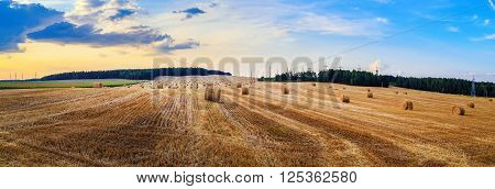 Hay bales on field. Autumn field with hay bales after harvest. Rural landscape with haystacks against the backdrop of a beautiful sunset sky. Panorama shot.