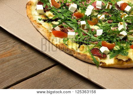 Appetizing pizza with ham, salami, arugula, cherry tomatoes, fetaksa, balsamic closeup on wooden background