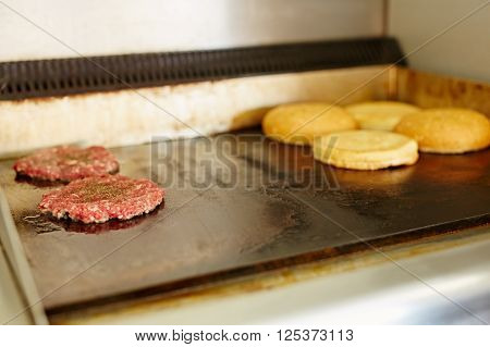Two burger patties frying next to each other with open buns being toasted nearby
** Note: Shallow depth of field