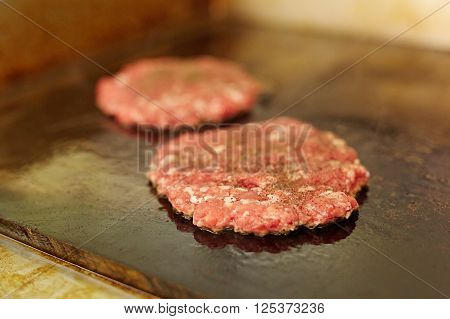 Fresh burger patties seasoning on top frying next to each other on a grill with
** Note: Shallow depth of field