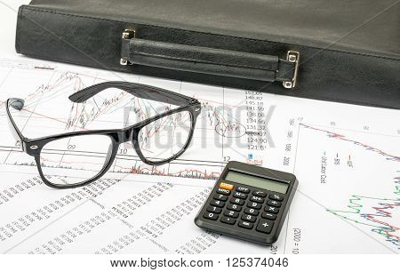 Glasses and suitcase with calculator on grpahical charts background, business concept