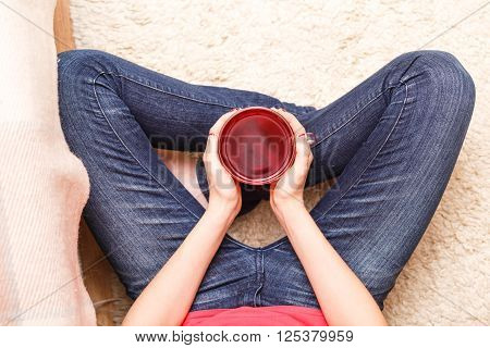 Teenage girl holding cup of tea sittng on the floor. Top view image