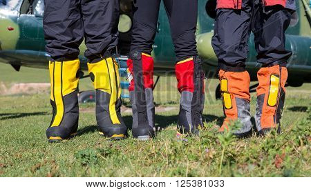 High Altitude Mountain Boots Three People Staying on Grassy Meadow with Cargo Helicopter on Background