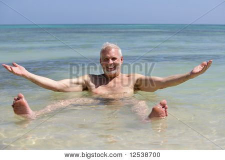 Portret van een glimlachende man badend in de zee met armen omhoog