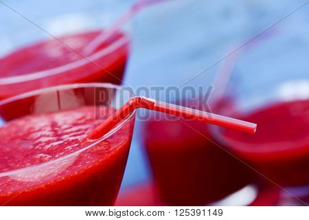 closeup of some cocktail glasses with fresh red smoothies, against a blue background