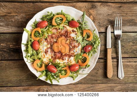 breakfast omlet with sausage and tomatoes and paprica surrounded by rocket salad on wooden table with fork and knife