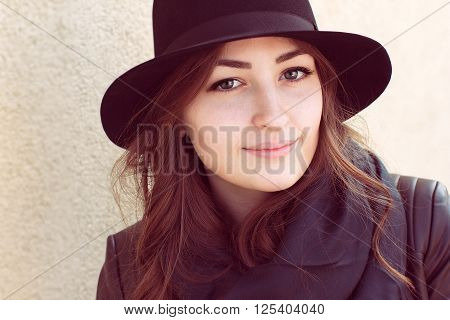 portrait of a girl with green eyes and foxy hair in a black hat and scarf standing near light wall and looking at the camera