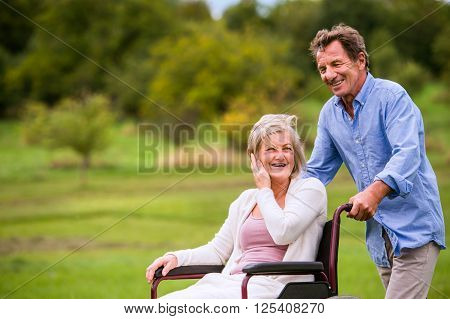 Senior man pushing woman sitting in wheelchair oustide in green autumn nature